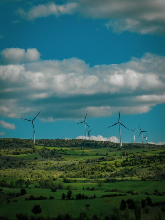 Scenic view of wind turbines on lush green hills with a bright blue sky and clouds.